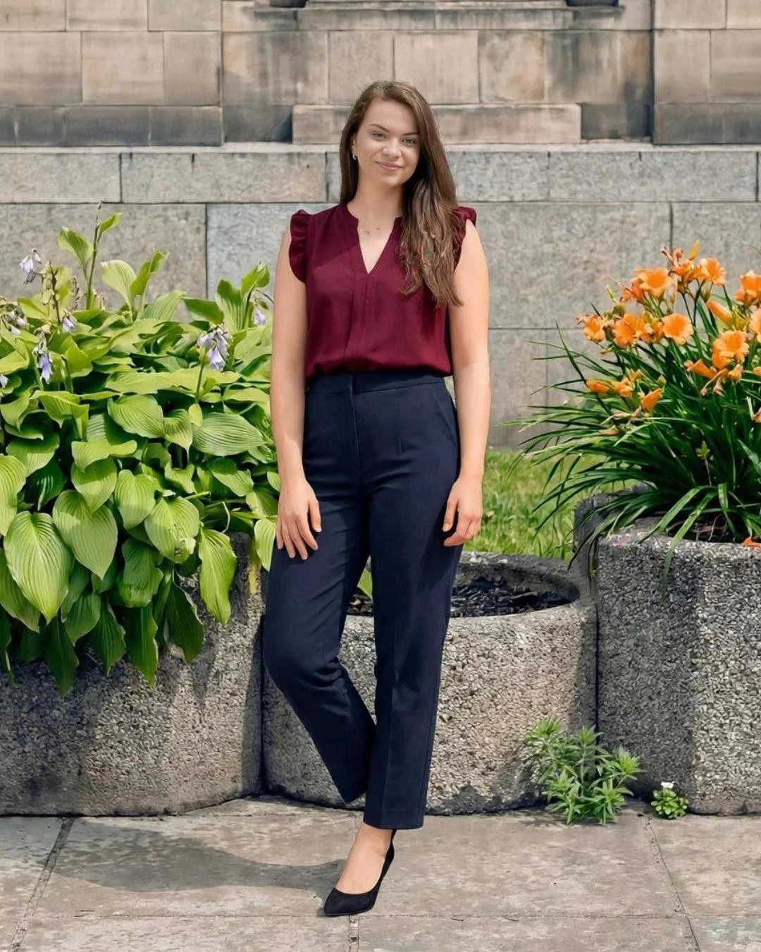 A burgundy sleeveless top with navy tailored trousers and black pumps