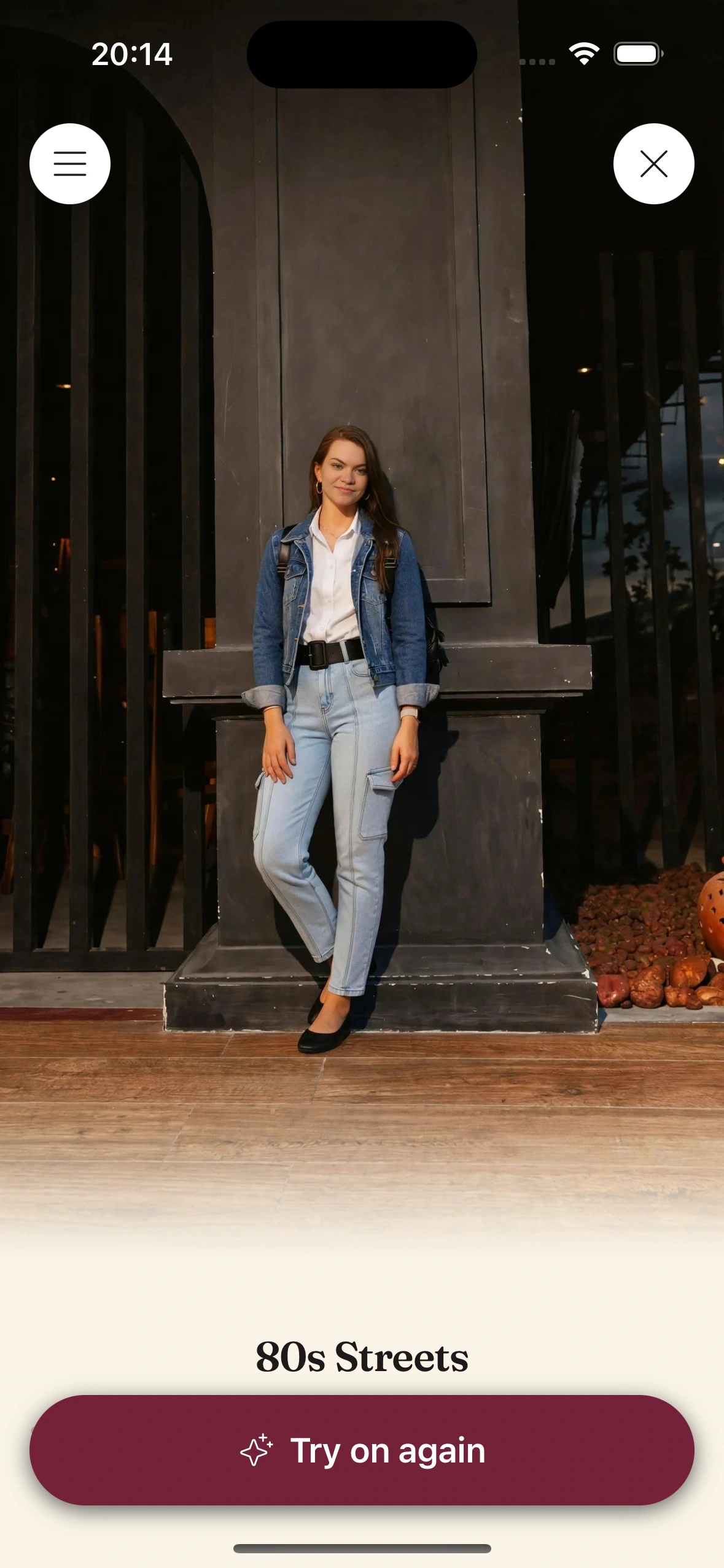 A virtual try-on render of a woman in a denim jacket with the sleeves pushed up over a white shirt, a wide black belt at the waist, high-waisted light-wash tapered jeans and black flats