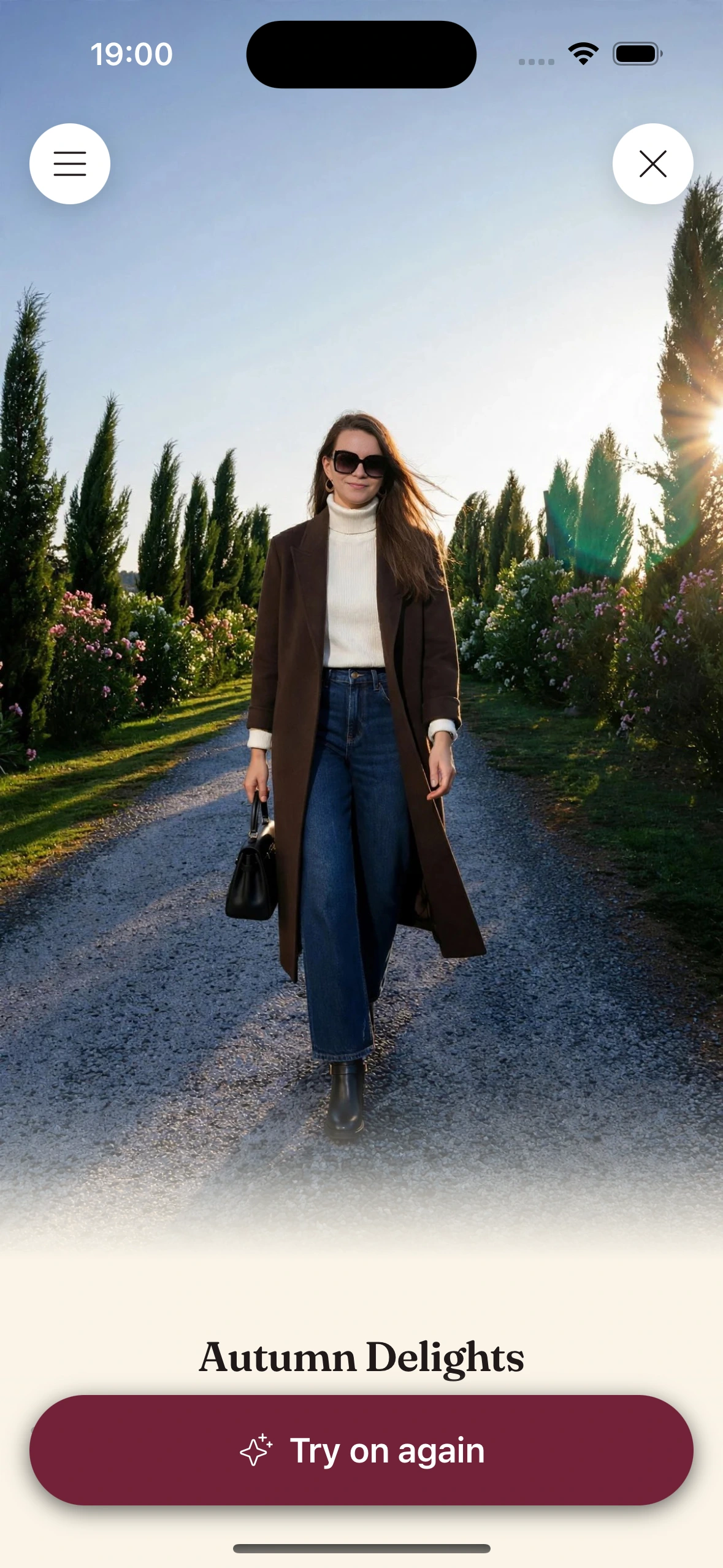 A virtual try-on render of a woman in oversized black sunglasses, a long brown coat over a cream turtleneck, wide dark jeans and black ankle boots, walking down a cypress-lined gravel path